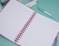 Open lined notebook pages with pink spiral coil; pens and notes beside it.