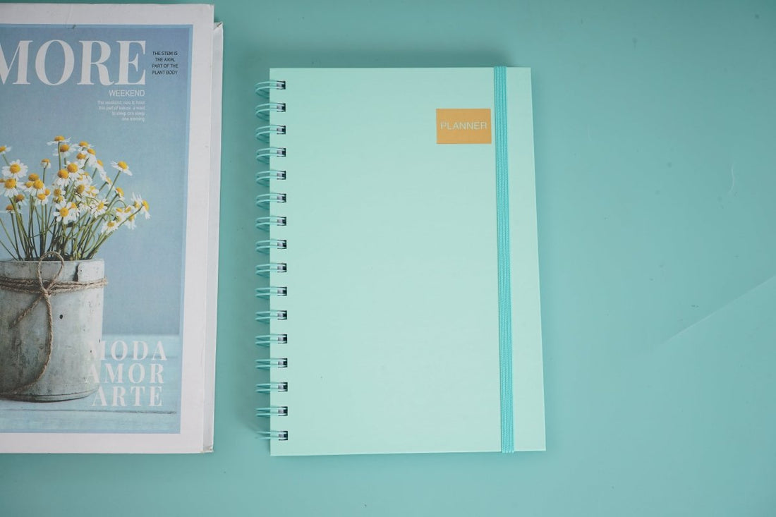 A5 daily planner notebook with turquoise cover, spiral coil binding, and gold label