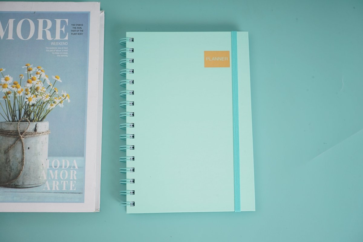 A5 daily planner notebook with turquoise cover, spiral coil binding, and gold label