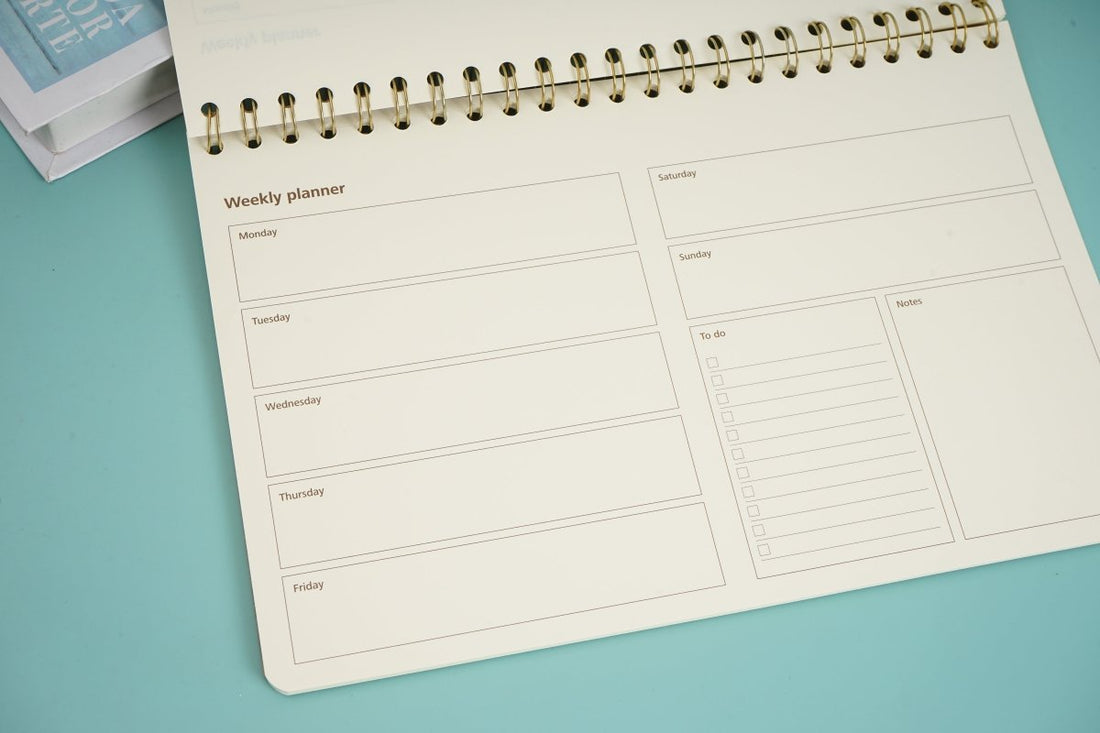 Weekly planner notebook open to dated weekly layout with printed boxes and lines