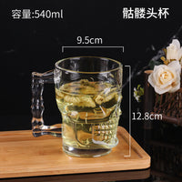 Clear glass skull mug with right handle, filled with tea and floating flowers