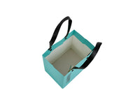Open turquoise gift bag with black handles and beige interior lining