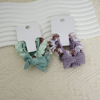 Fabric scrunchie hair ties, teal and lavender ruffled bands with small logo patch on card.