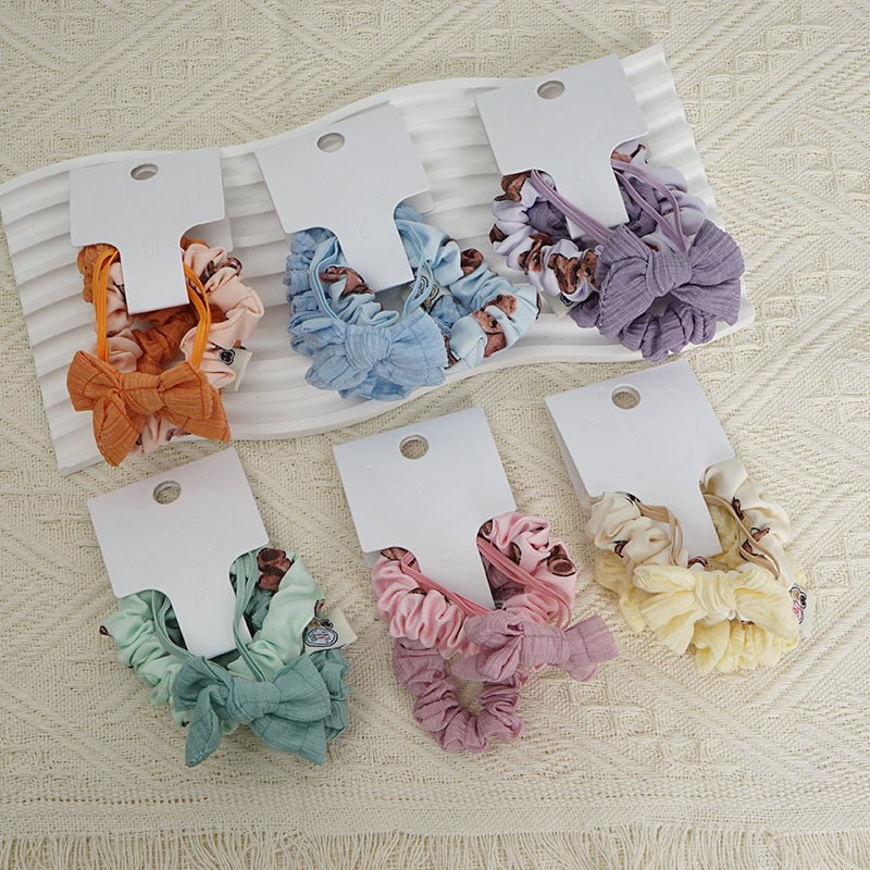 Assorted fabric scrunchie hair ties in orange, blue, purple, green, pink, and cream.