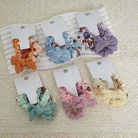 Assorted fabric scrunchie hair ties in orange, blue, purple, green, pink, and cream.