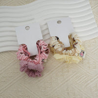 Fabric scrunchie hair ties, pink and cream ruffled bands with small logo patch on card.