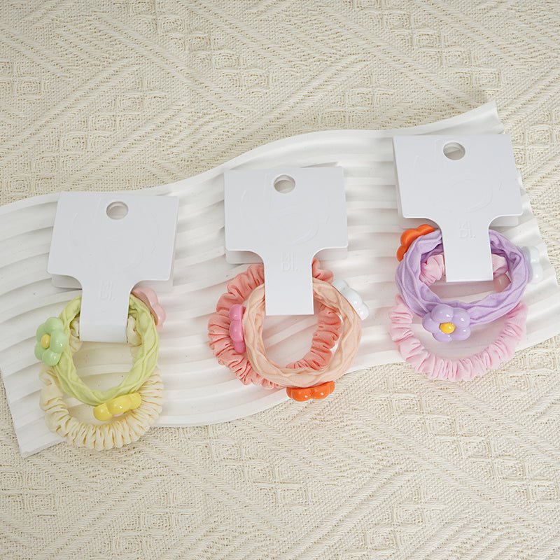 Flower hair ties set with ruffled fabric loops in green, peach, purple, and pink on cards