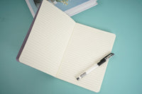 Lavender velvet notebook open to simple lined pages with silver pen