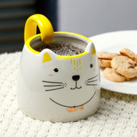 White ceramic cat-face mug with yellow handle, dark beverage inside