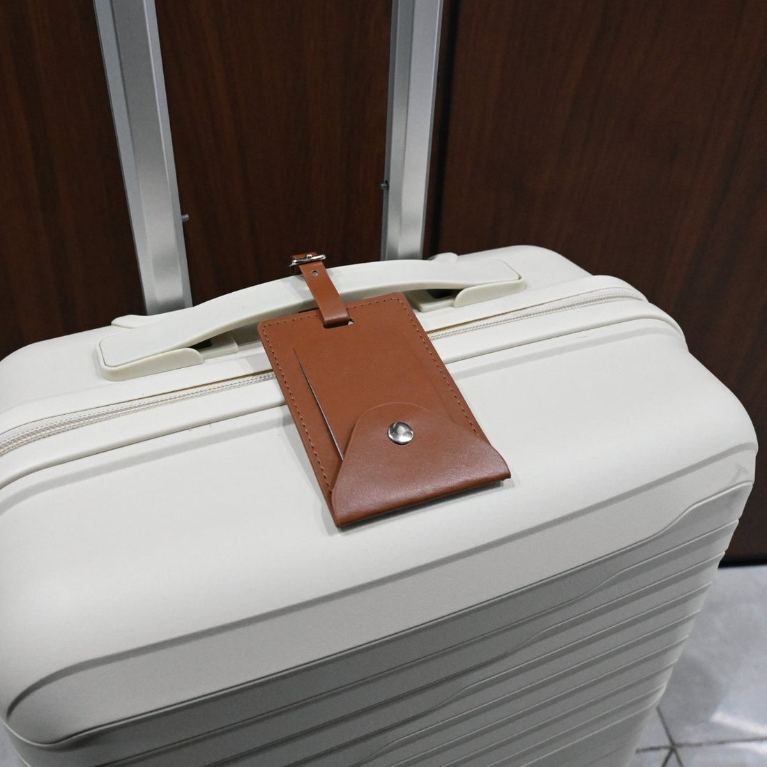 Leather luggage tag attached to a white suitcase with a metal button