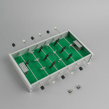 Mini desktop soccer game table with green field, foosball-style players, corner goals