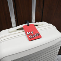 Red “MY BAG!” luggage ID tag attached to a white suitcase with black strap.