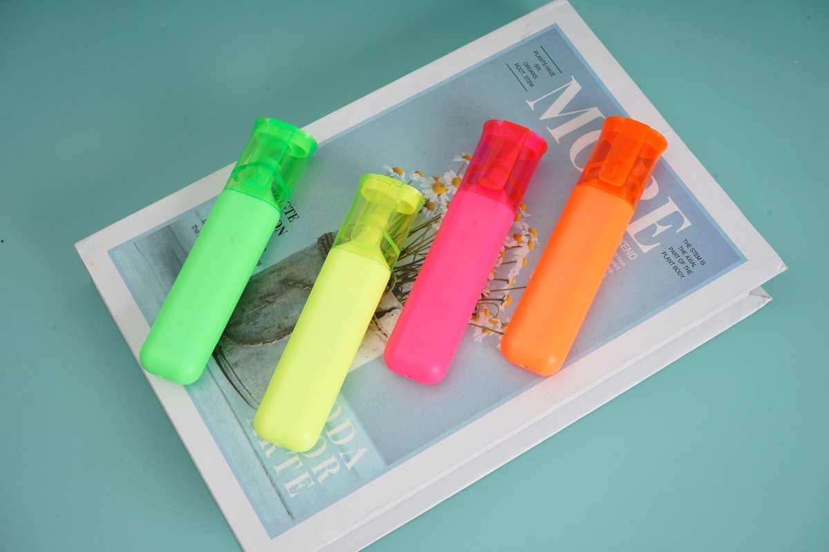 Neon highlighters lying on a brochure, green, yellow, pink, orange, chisel tips.