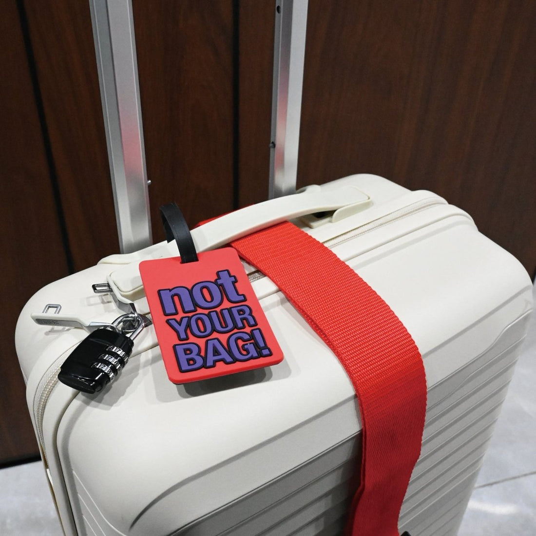 White suitcase with red strap and red "not YOUR BAG!" luggage tag