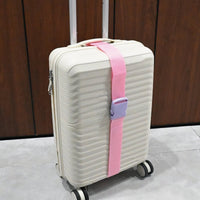 Pink luggage strap attached to a white suitcase, with gray attachment pieces and webbing.