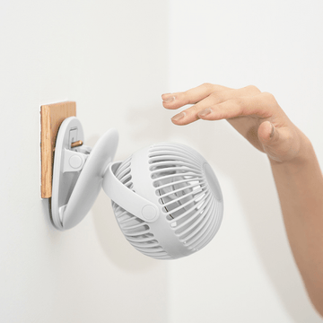 Portable mini clip fan with gray round grille and clip mount on wall