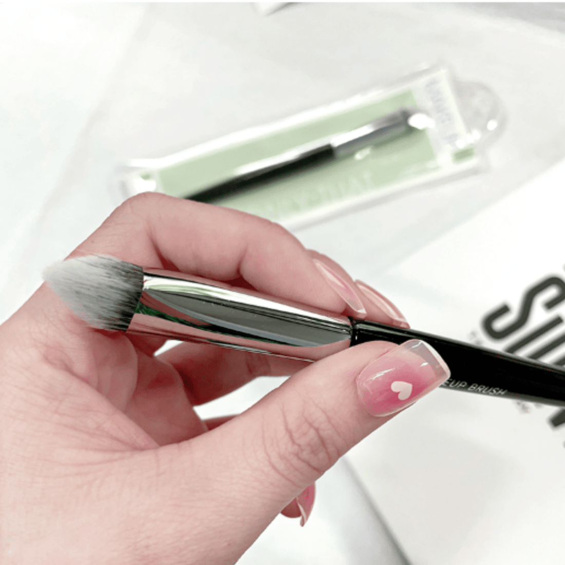 Makeup brush held in hand, black handle with angled white bristles