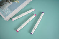Set of three purple-tipped highlighters lying on a flat surface