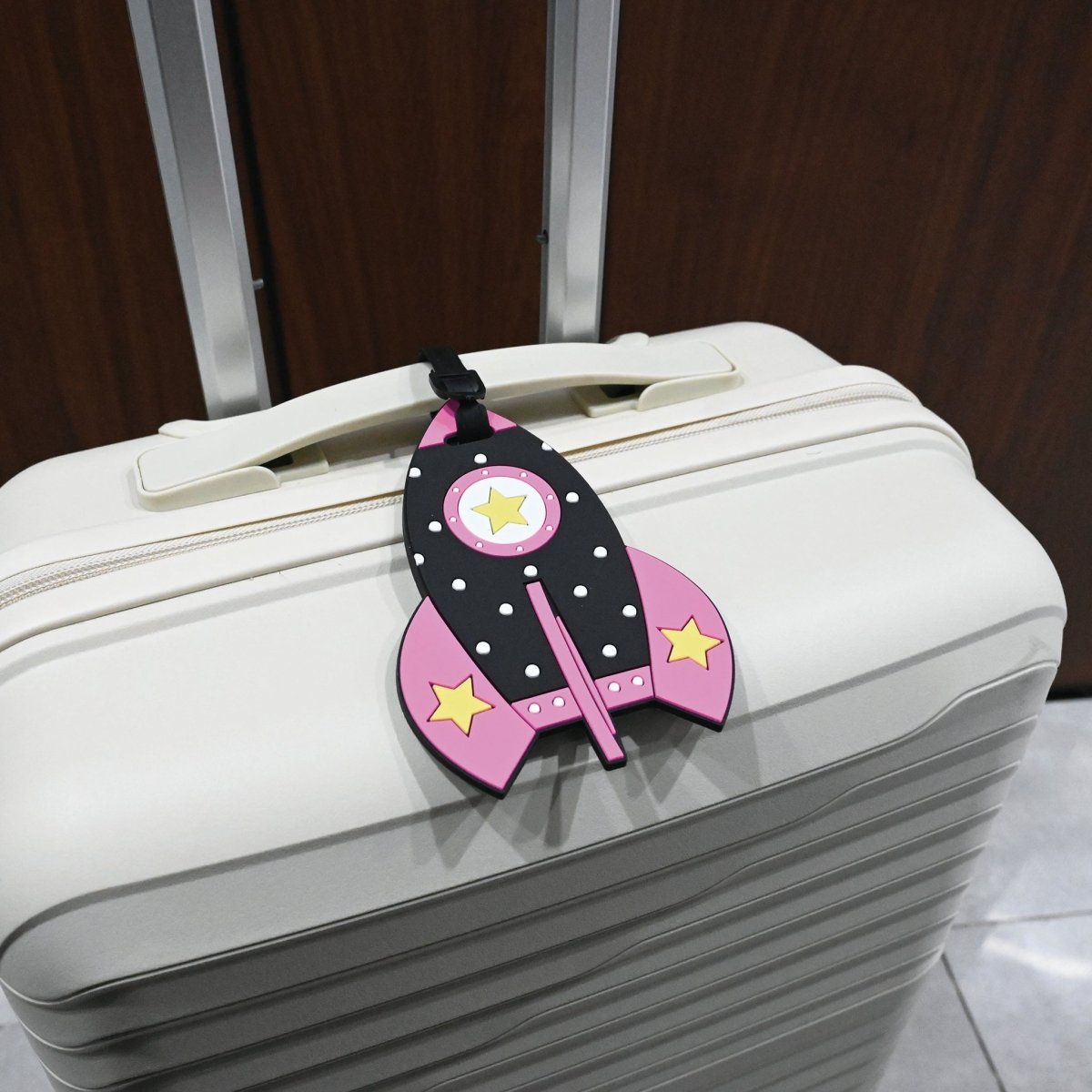 Pink rocket-shaped kids luggage tag with black strap on a white suitcase