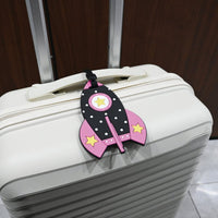 Pink rocket-shaped kids luggage tag with black strap on a white suitcase