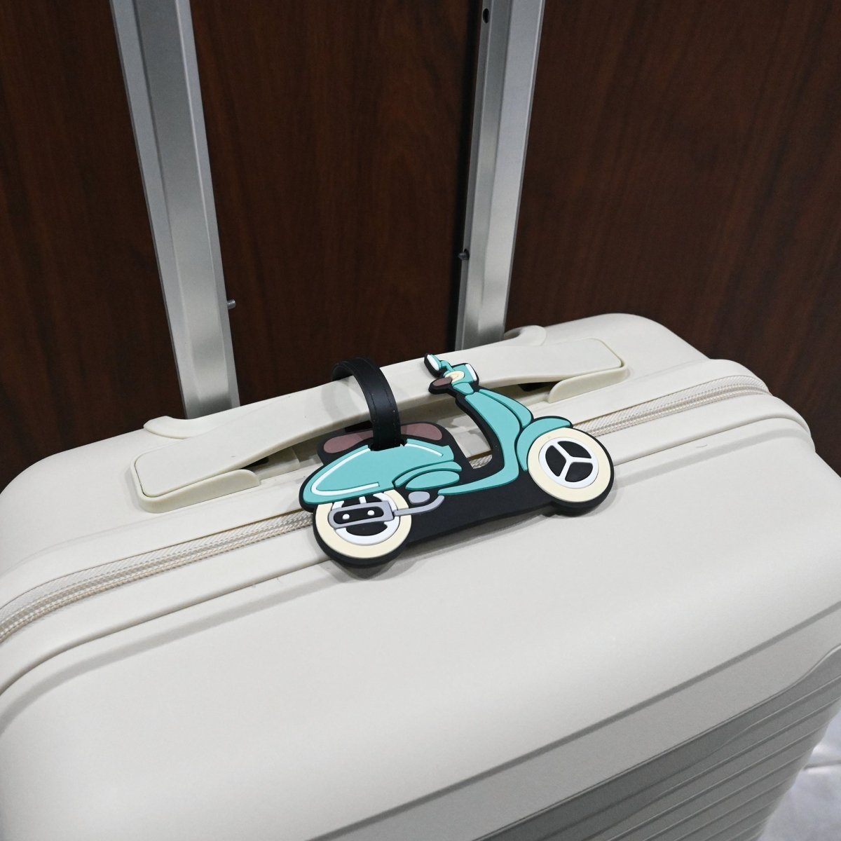Scooter luggage tag on a light suitcase with black strap and teal scooter design
