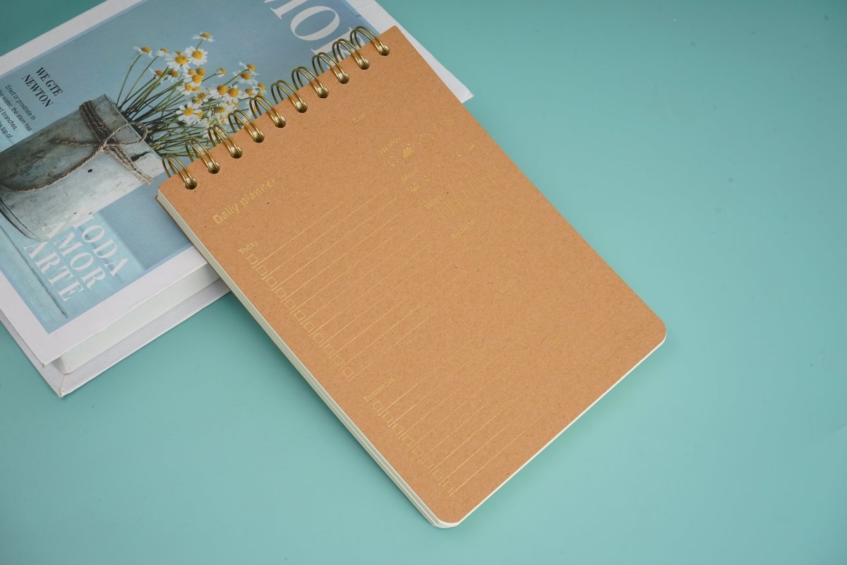 Wood-grain coil notebook with tan cover and gold spiral rings, lying closed
