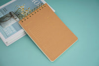 Wood-grain coil notebook with tan cover and gold spiral rings, lying closed