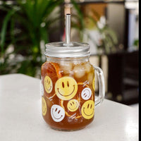 Clear smiley mason jar mug with handle and straw; yellow and white faces with drink inside