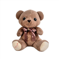 Soft brown teddy bear plush with mauve ribbon bow and stitched muzzle.