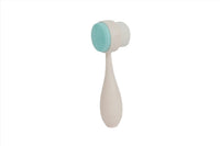 Light teal face cleansing brush with soft round bristles and curved handle