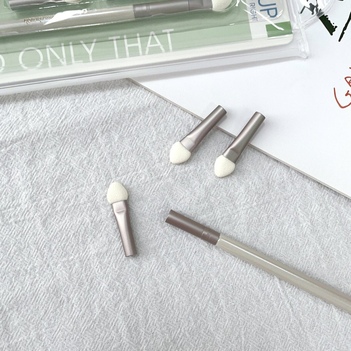 Three sponge eye shadow applicators with taupe handles and white sponge tips on textured surface
