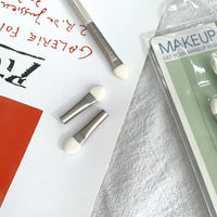 Three sponge eye shadow applicators with taupe handles and white sponge tips, blister pack nearby