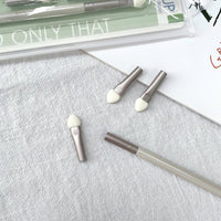 Three sponge eye shadow applicators with taupe handles and white sponge tips; one lies diagonally