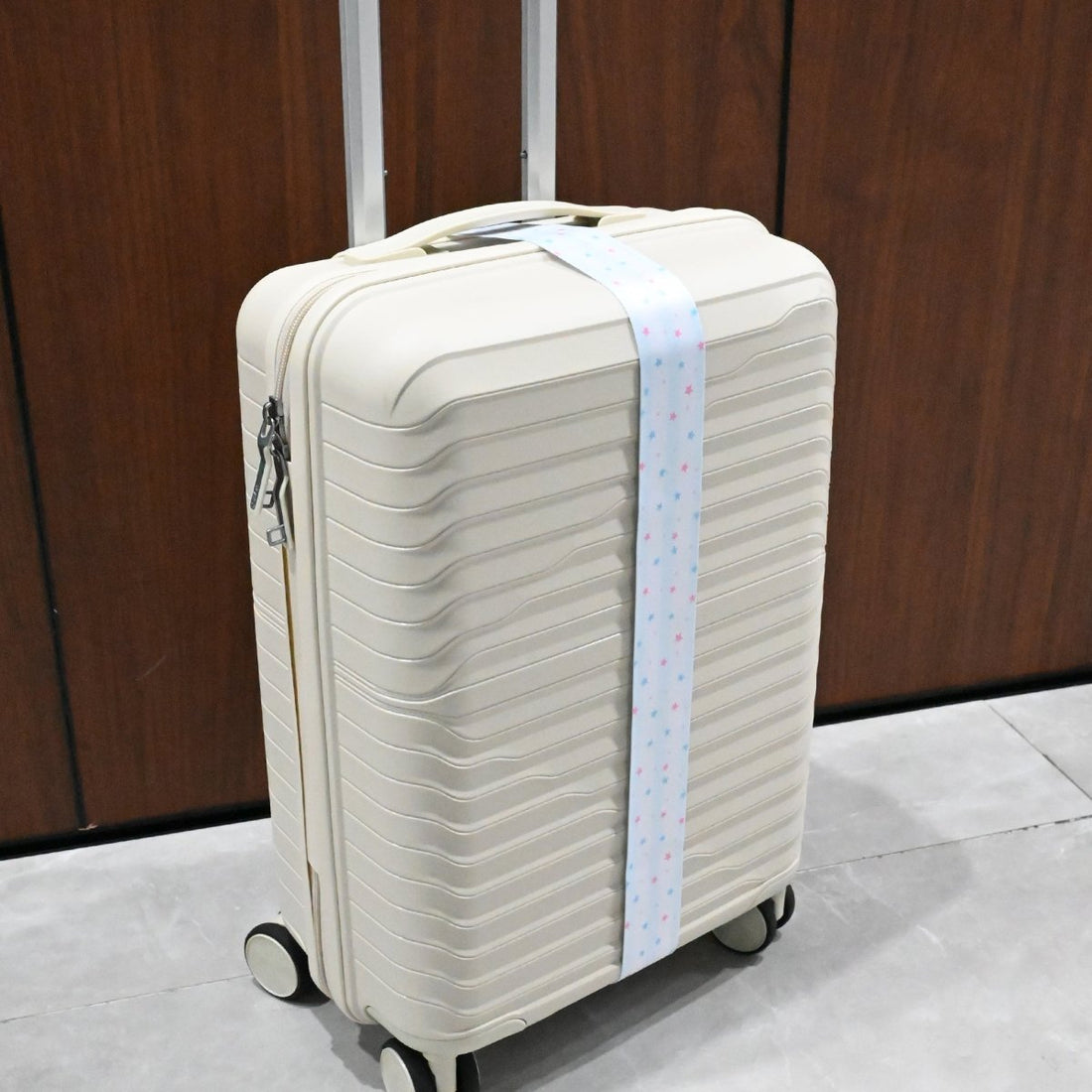 Star print luggage strap attached to a white rolling suitcase with black hardware