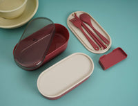 Maroon bento lunch box with separate lid, fork, spoon, and knife