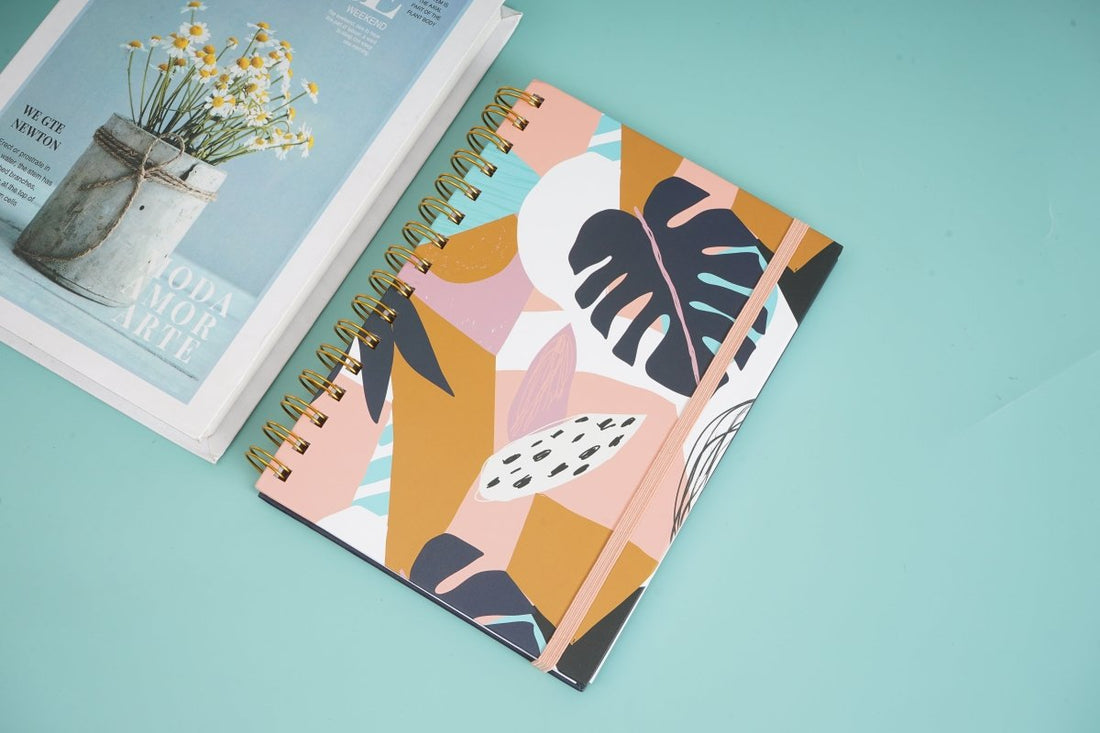 A5 spiral notebook with botanical leaf cover and gold coil binding, angled