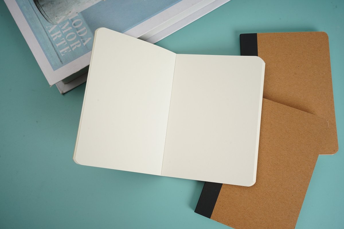 Kraft paper notebook opened to white pages, showing interior leaves and brown back cover.