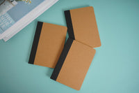 Kraft paper notebook with brown covers and black elastic strap, angled view.