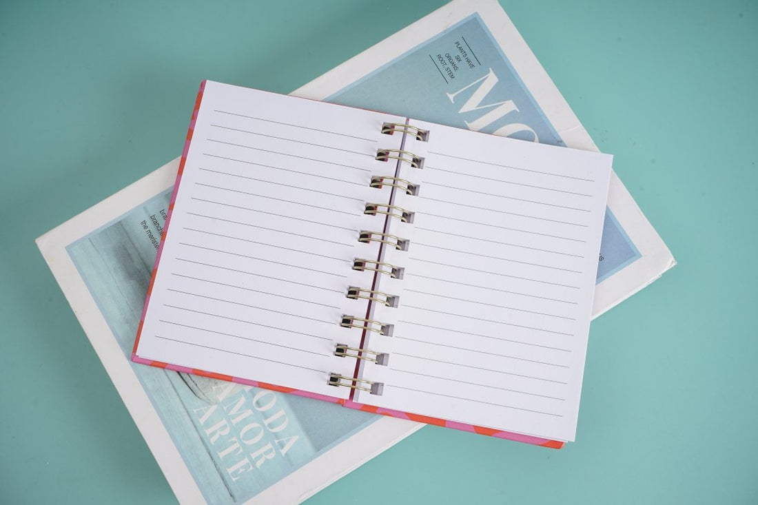 Open notebook with white lined pages and metal spiral rings, orange edge binding