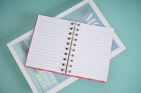 Open notebook with white lined pages and metal spiral rings, orange edge binding