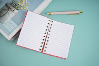 Open lined notebook with metal spiral rings and gold pen resting on top