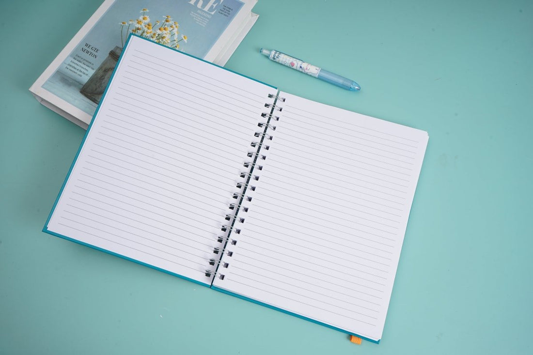 Open coil notebook with white lined pages and black spiral rings, blue cover edges