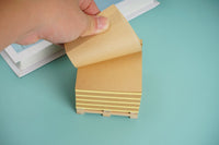 Hand lifting a memo note from a wooden memo pad with twine-tied stacked sheets