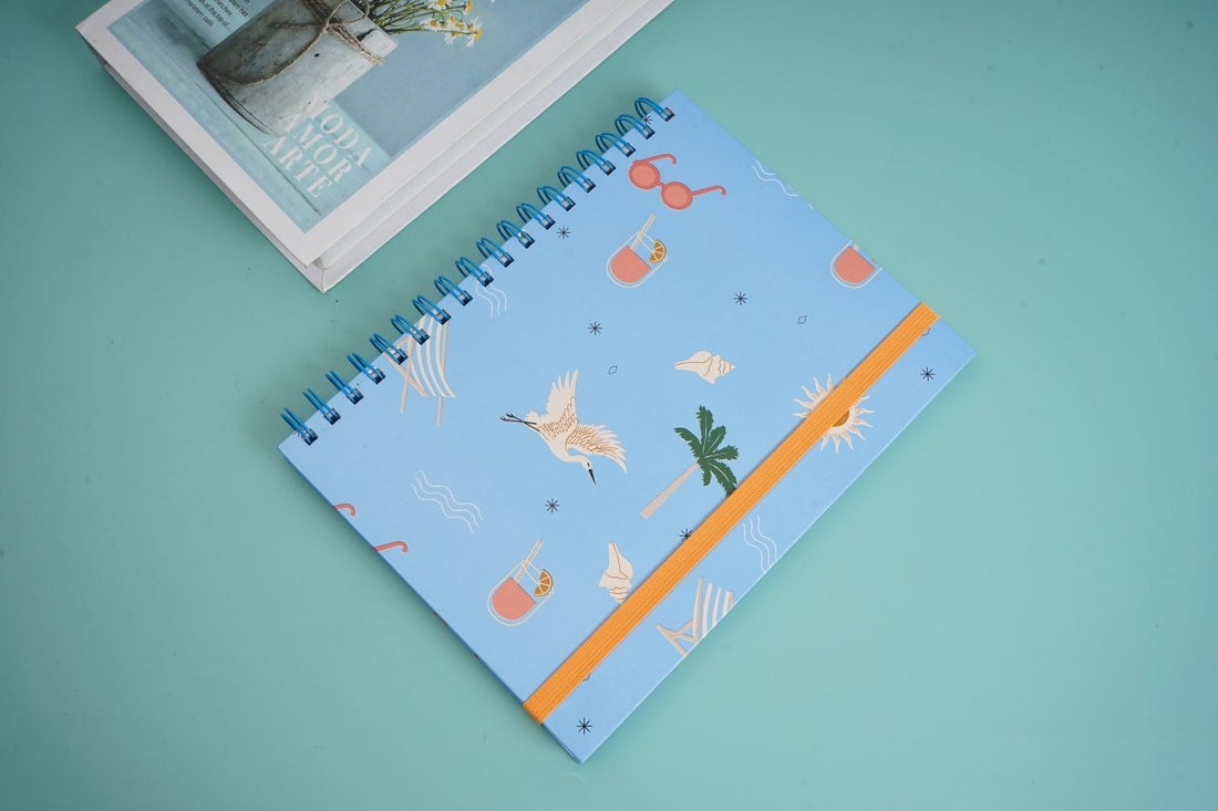 Kids blue coil notebook angled view, beach graphics, orange trim and spiral binding