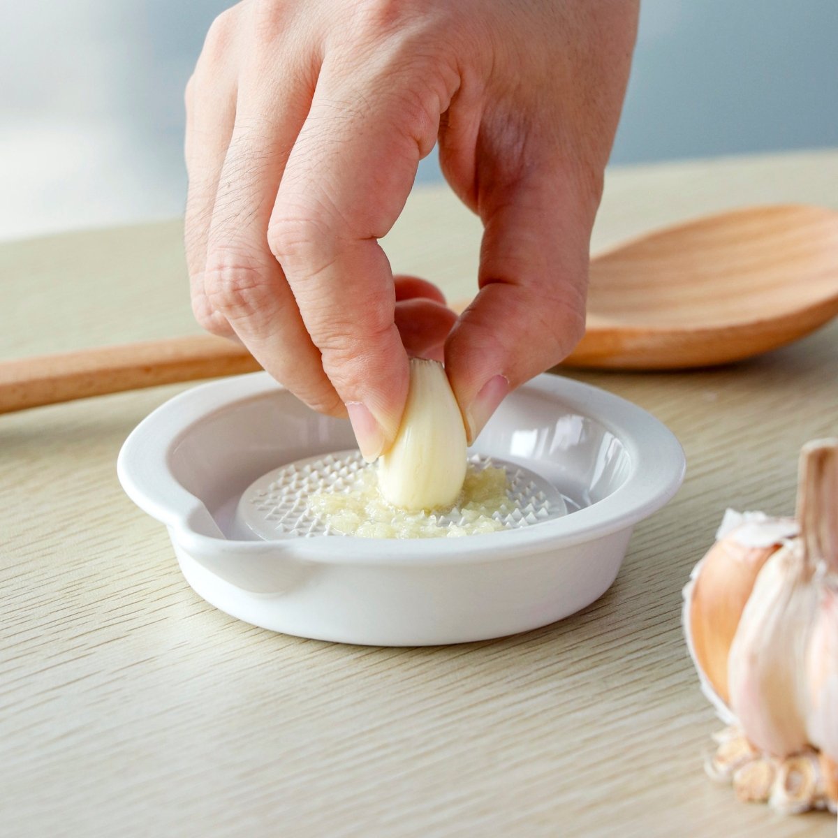Hand placing garlic on textured ceramic spoon rest; wooden spoon rests nearby