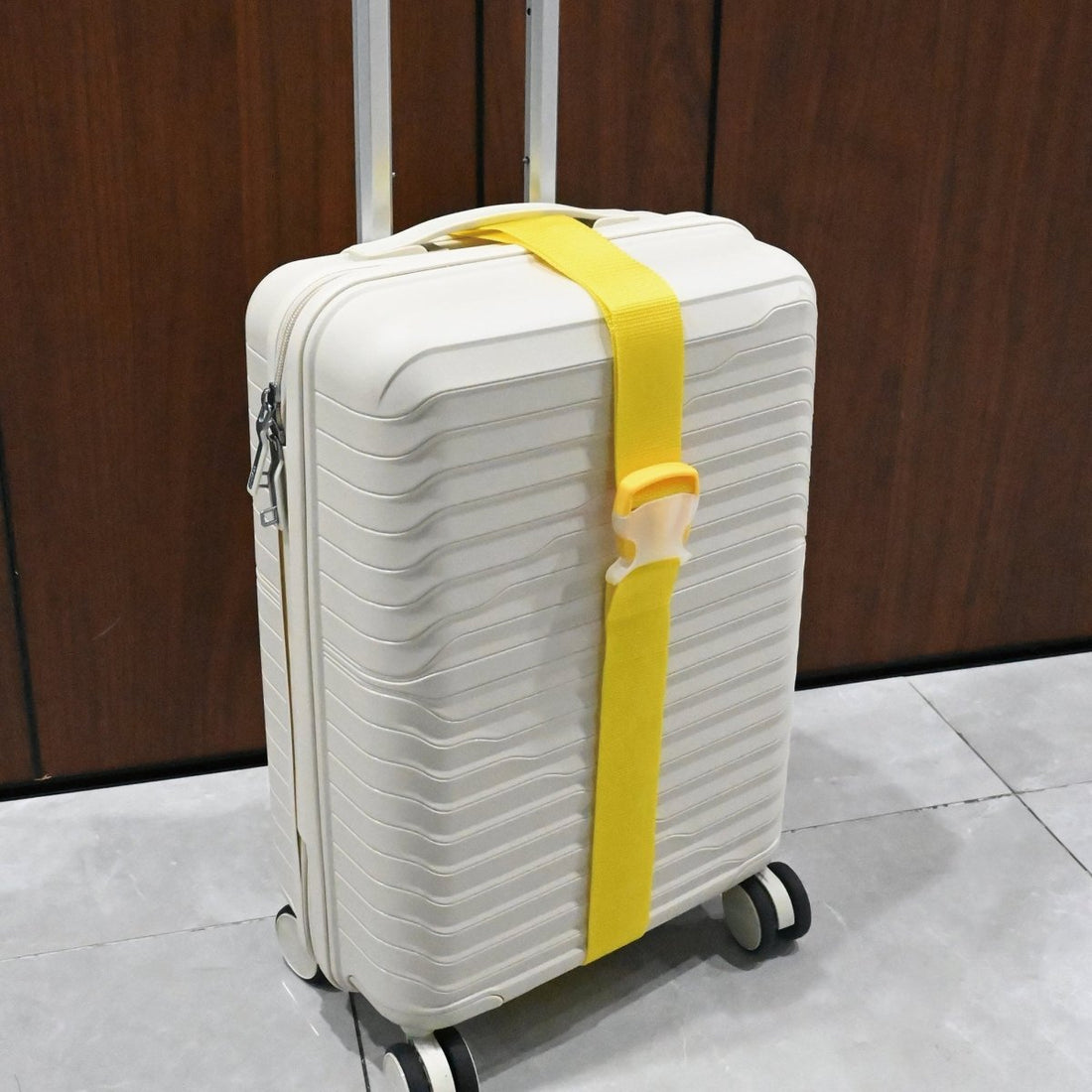 Yellow luggage strap wrapped around white suitcase with wheels