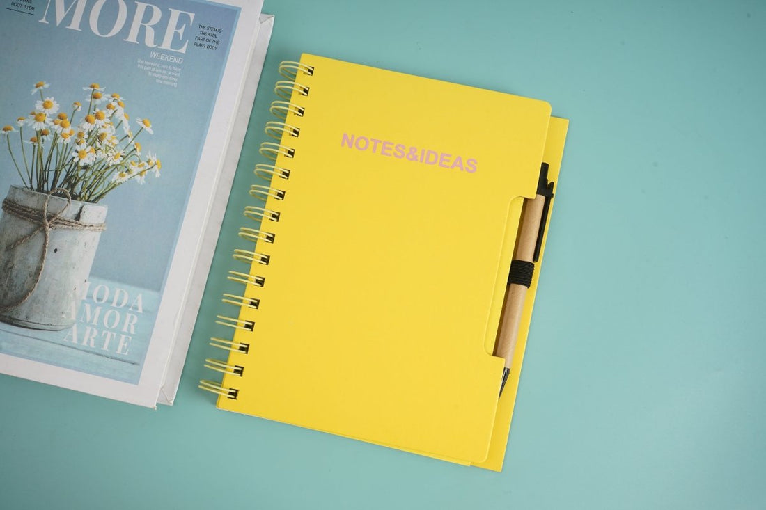 Yellow spiral notebook with pen clipped on cover, notes and ideas title